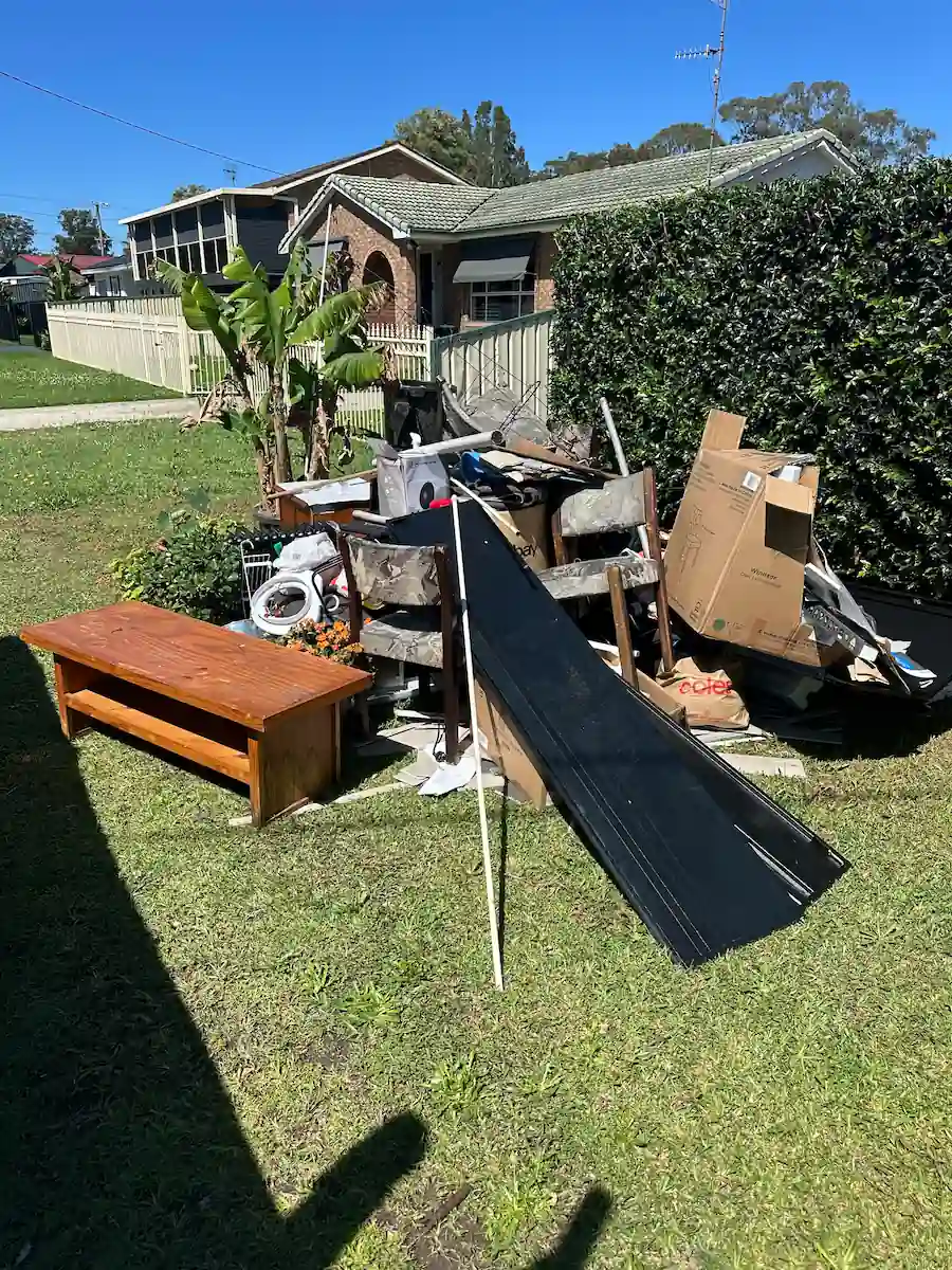 Old couch, junk, and a sheet on the grass out front of a Central Coast home, showing home rubbish removal under clear skies.