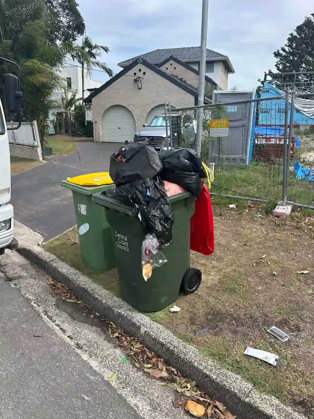 home rubbish removal by RubbishGo: overflowing bins with bags on a street, house in the background.