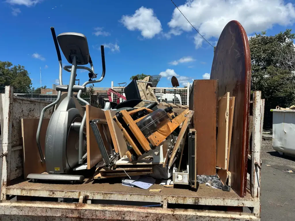Aussie home rubbish removal: truck loaded with treadmill, table, and junk under a clear blue sky.
