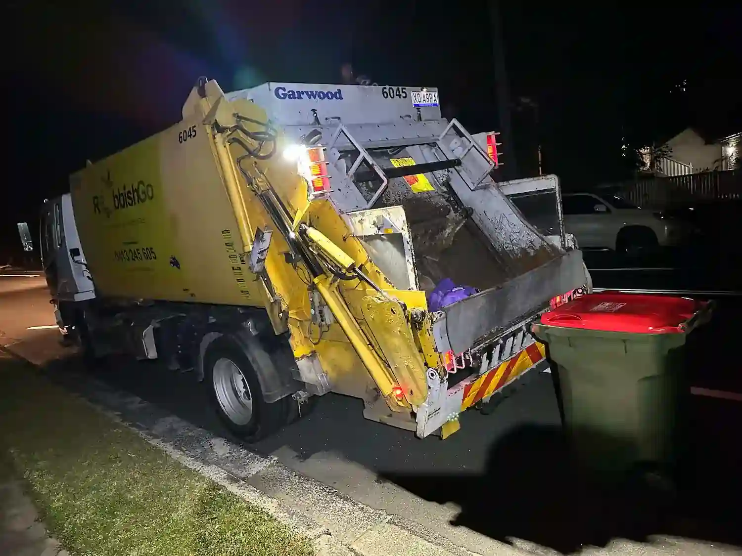 Aussie waste collection service: RubbishGo truck emptying a red bin on a dark street at night.