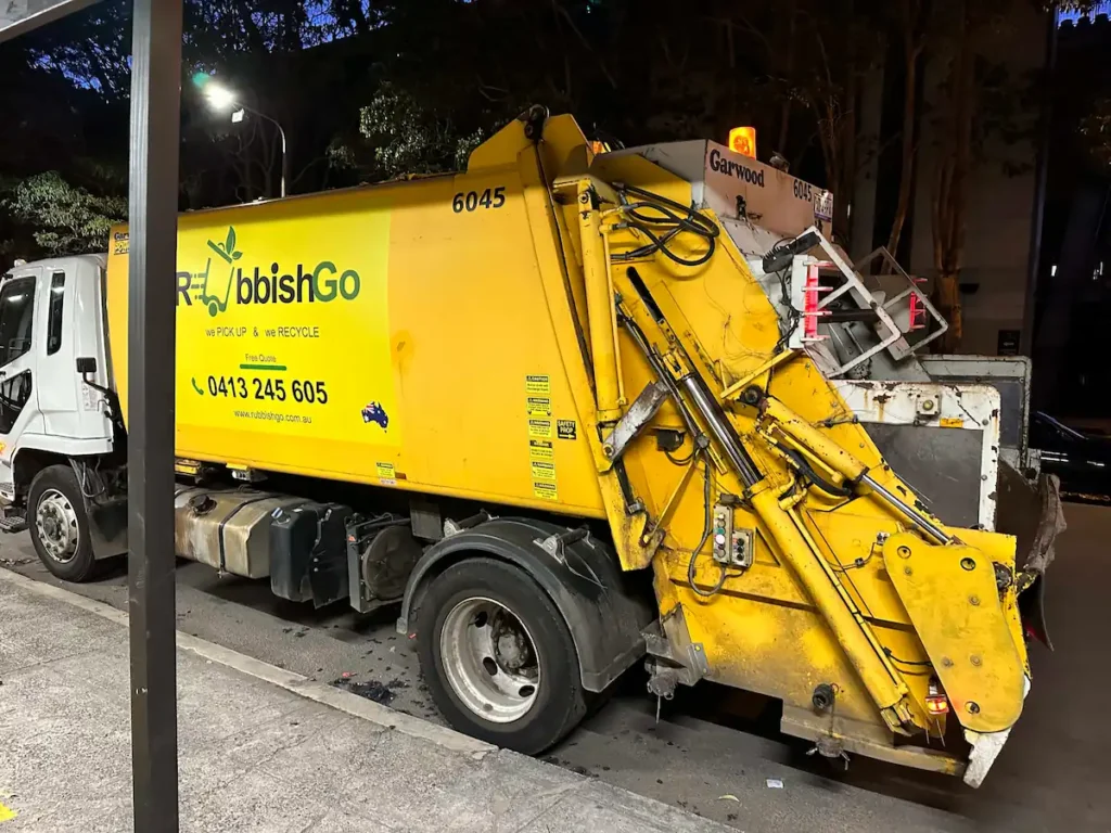 RubbishGo yellow truck handling hard rubbish collection on a quiet street at night.