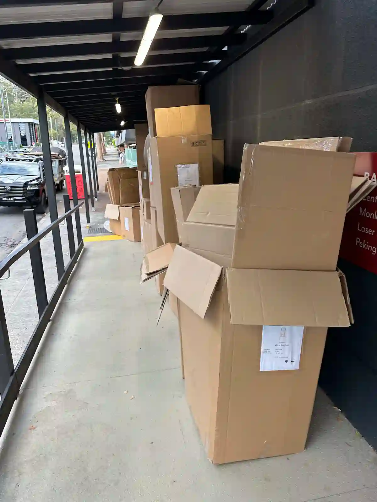 Aussie Commercial Rubbish Removal: stacks of cardboard boxes piled under a covered walkway in a busy Central Coast area.