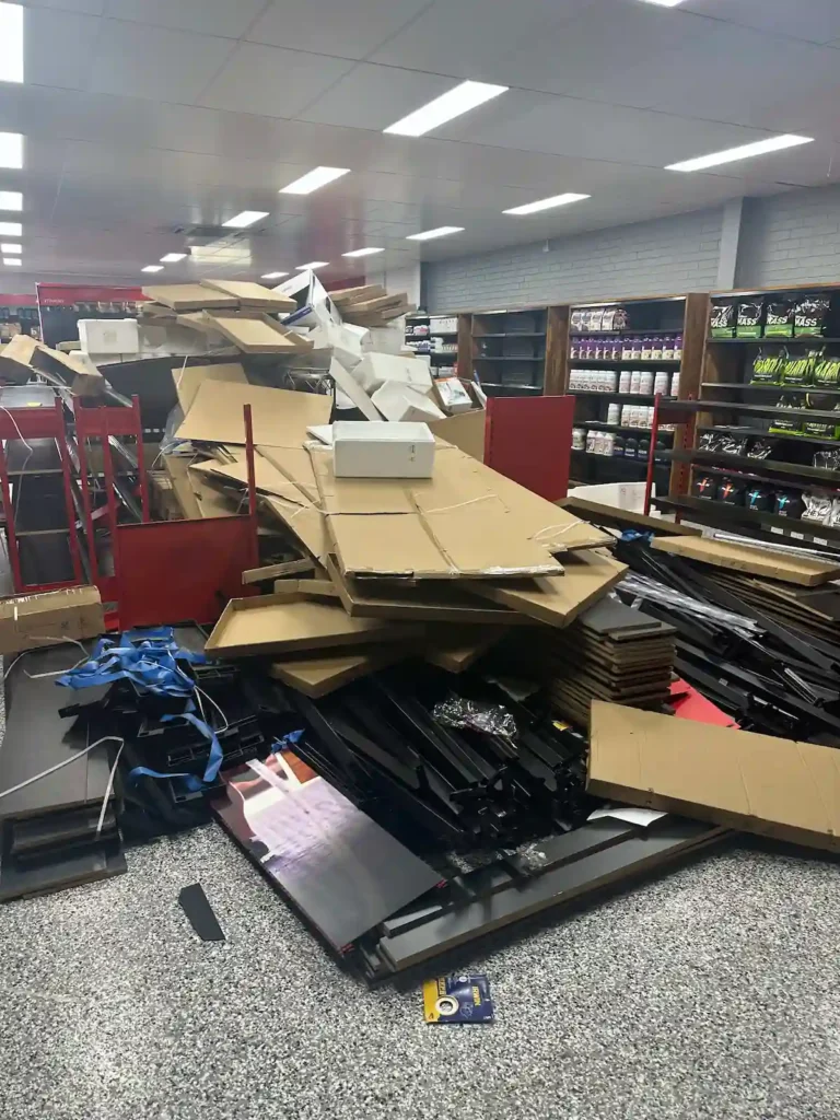 Chaotic stack of shelves and cardboard boxes in a lit warehouse, showing commercial rubbish removal by RubbishGo.