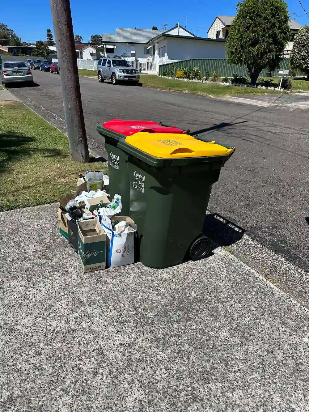 Green and yellow bins with bags and boxes on a quiet Central Coast street, showing an Aussie waste collection service.
