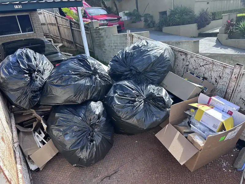 Collected household plastic waste packed in large black garbage bags, along with several cardboard boxes, ready to be transported to a recycling centre.