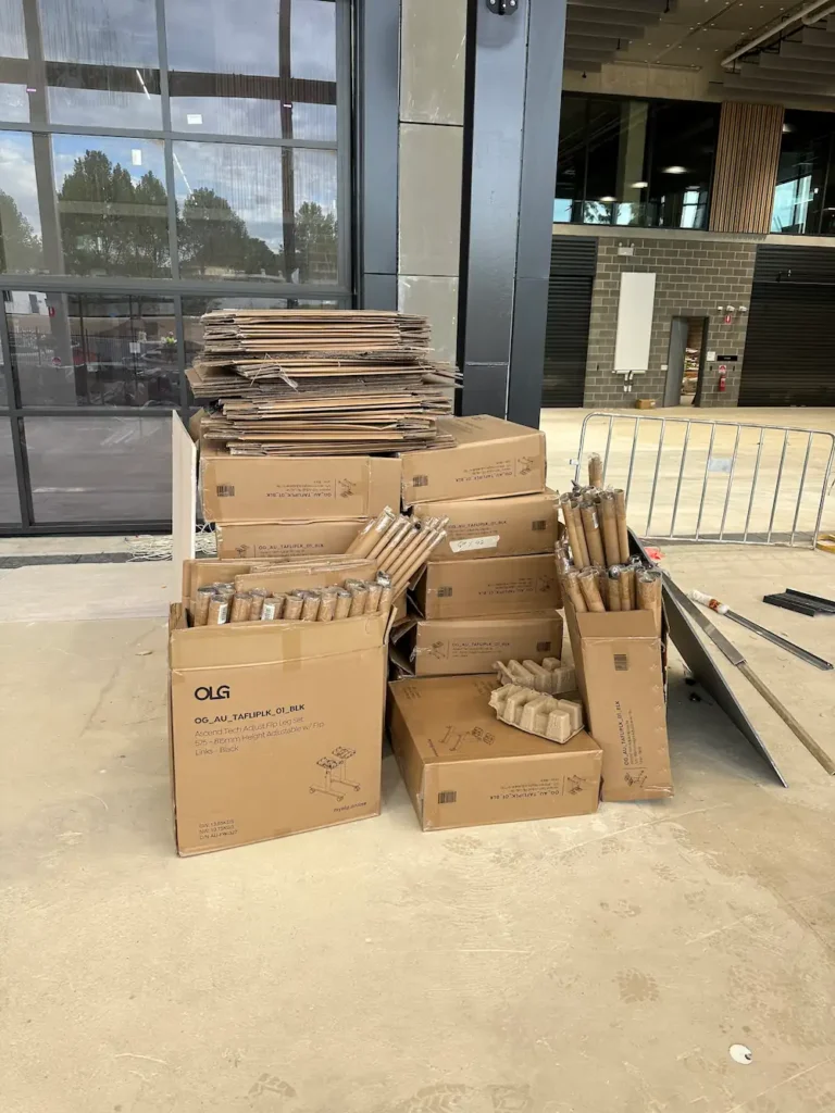 A large pile of empty cardboard boxes and cartons stacked outside an industrial warehouse, ready for commercial waste collection and recycling.