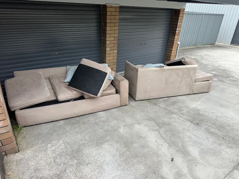 "A few old cream-colored sofas abandoned near a garage door, ready to be collected by a furniture removal team."