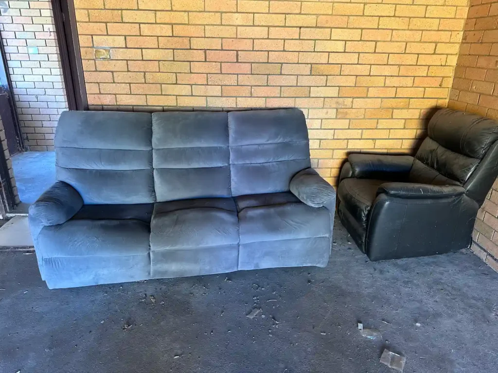 A grey sofa and a black leather couch in a room, ready to be disposed of soon and sent to recycling centres.