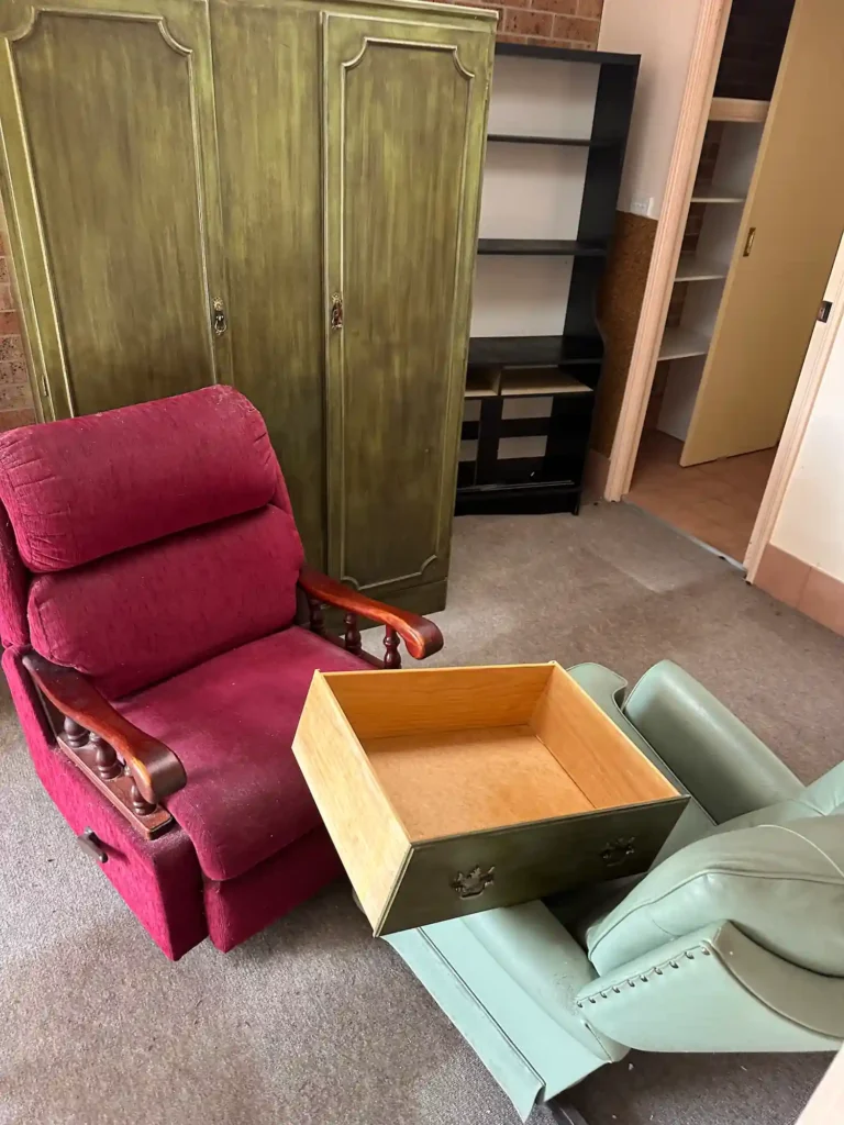 Two armchairs, one red and one green, next to an old green wooden cabinet with a drawer on the chair, being packed for disposal.