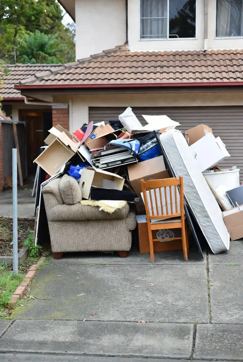 "Pile of miscellaneous end-of-lease items outside a house including old sofa, mattress, and cardboard, ready for RubbishGo collection."